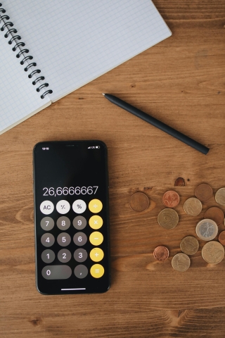 Image of calculator app on phone along with changes lying around and financial paper.